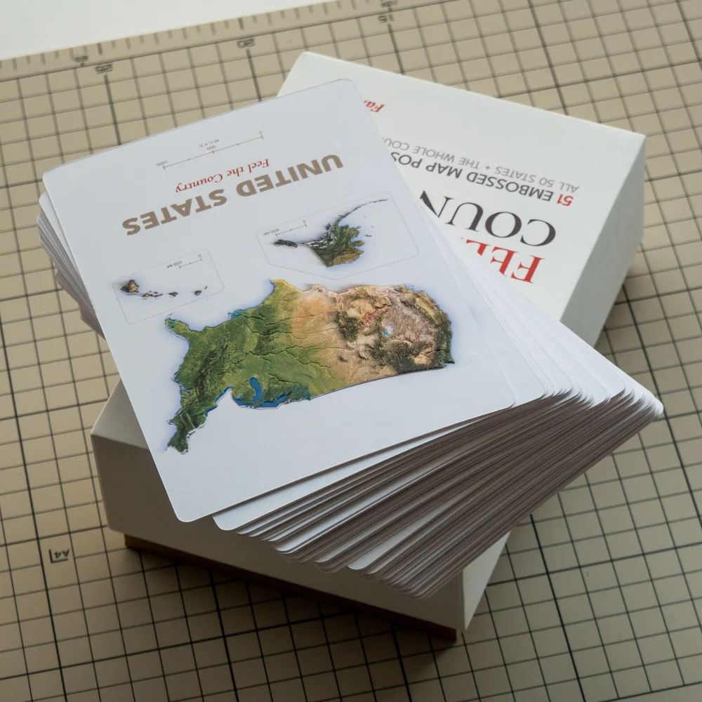 A fanned stack of proof postcards resting on the box base, with the lid behind