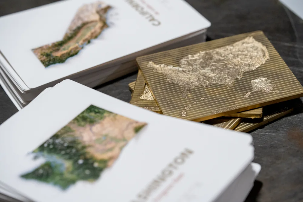 Metal embossing dies beside finished Far Maps postcard production proofs in the workshop