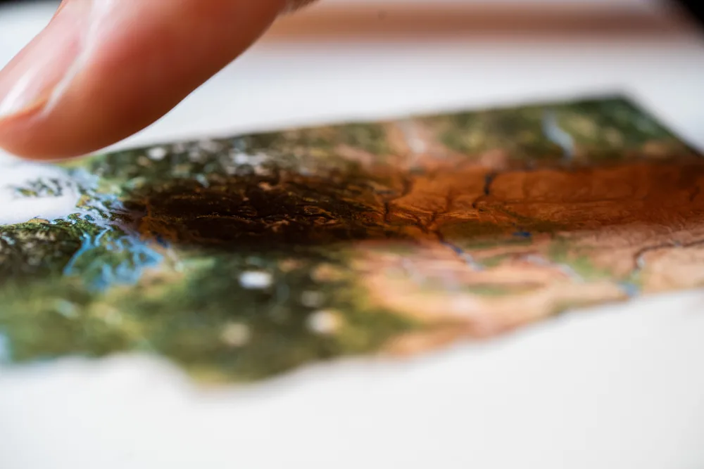 Fingertips touching the embossed mountain ranges on a United States postcard production proof