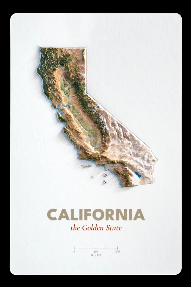 California production proof photographed straight on, the raised terrain standing off a white card above the printed state name
