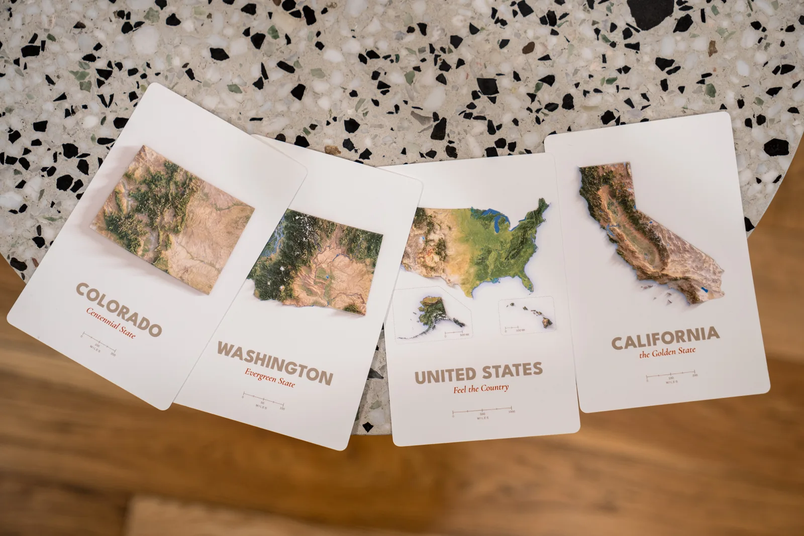Four Far Maps production proofs for California, Washington, Colorado, and the United States arranged on a table