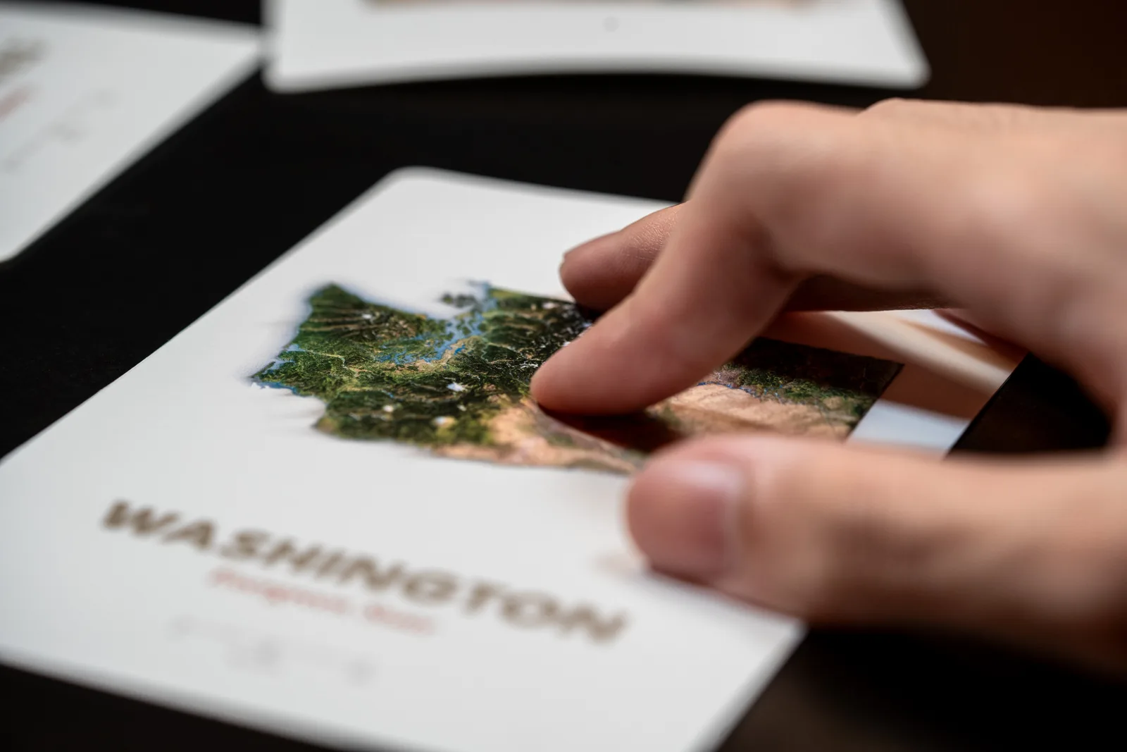 A fingertip touching the raised terrain on a Washington relief postcard production proof